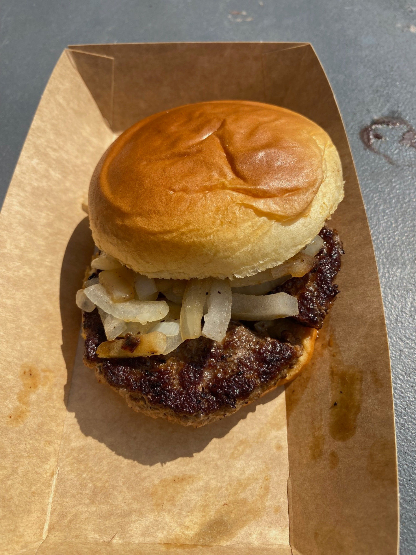 A charred burger with fried onions in a brown paper tray at the Robert Parker Stadium