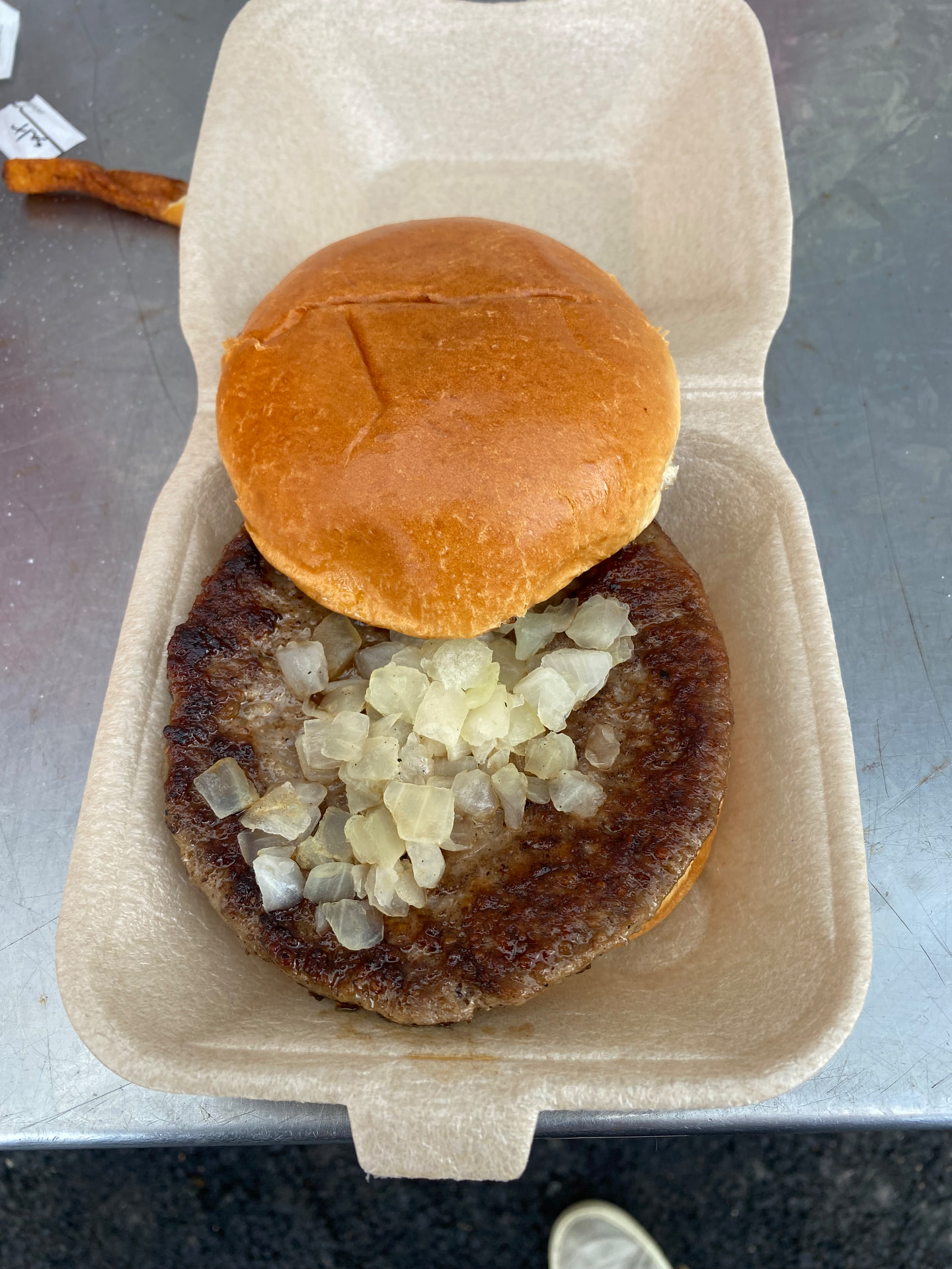 The opened Hampton & Richmond burger with a broad browned patty and chopped onions in a glazed bun