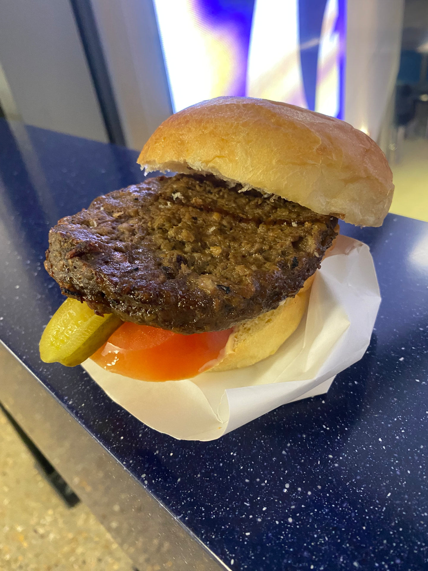 The opened venison Game Burger at the Tottenham Hotspur Stadium, with gherkin and tomato under a broad patty