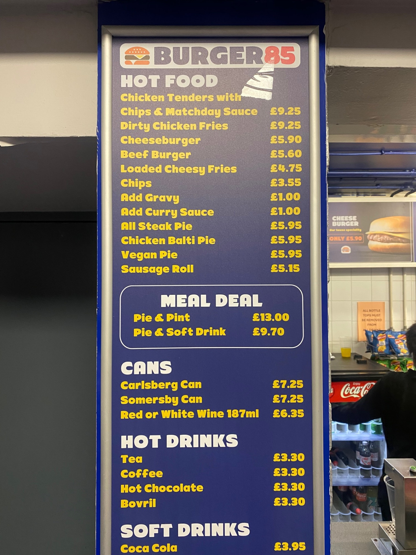 Burger85 price board at Loftus Road listing hot food, meal deal, cans and hot drinks prices